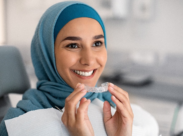 a woman putting clear aligners in her mouth in a dental office