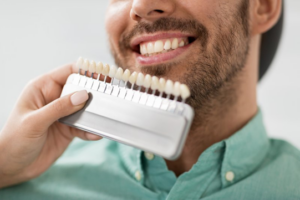 Close up of dentist holding set of dental veneers up to male patient’s smile